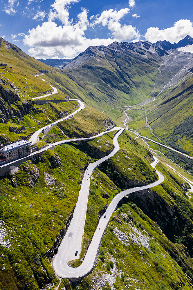 Cars driving along an Alpine road surrounded by green valleys and mountains