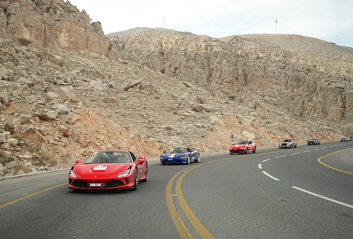 Luxury supercars cruising along spectacular mountain roads surrounded by breathtaking natural landscapes.