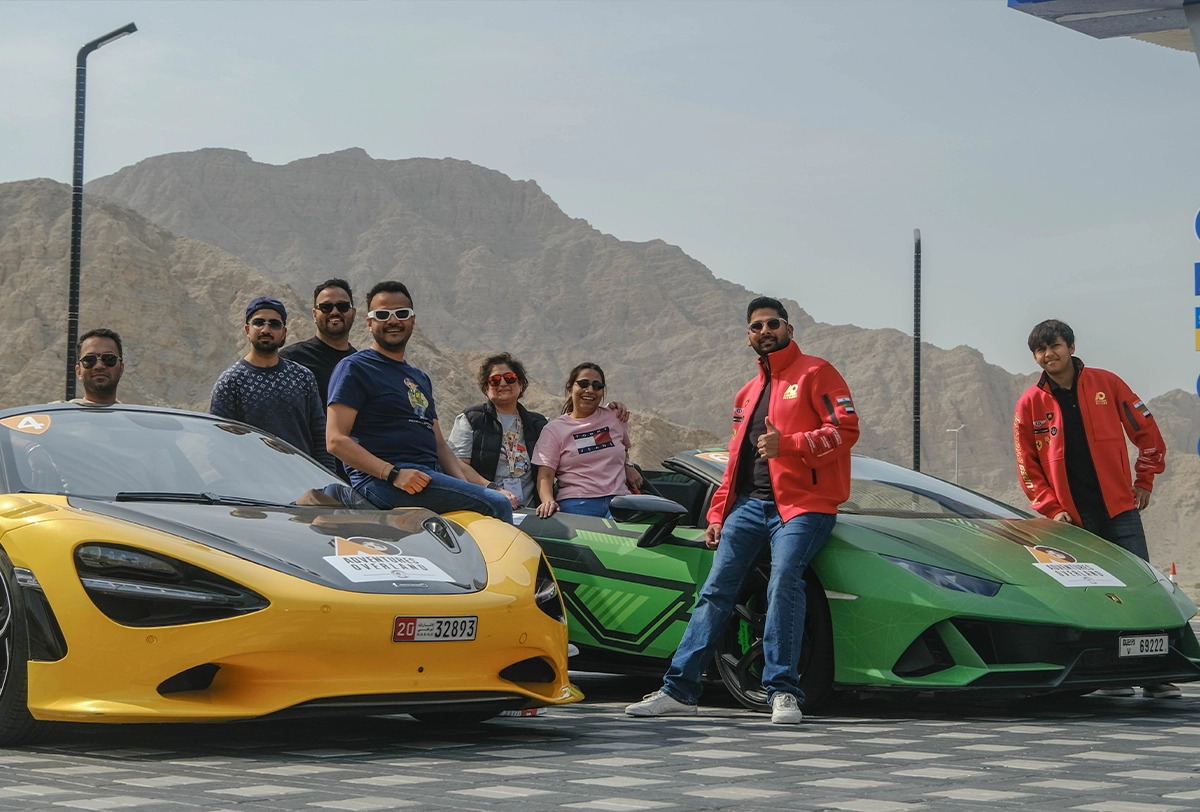 Posing with a stunning lineup of luxury supercars after an exhilarating day on the road.