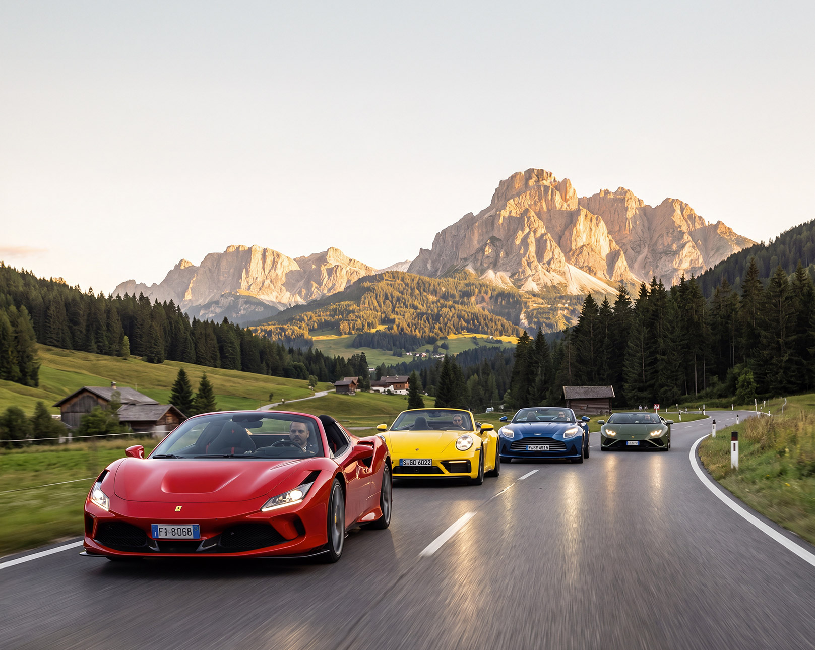Luxury supercars driving through the scenic European Alps on a mountain road.